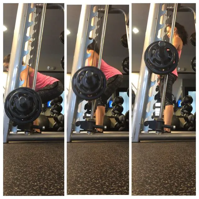 woman pink shirt performing a deadlift on a smith machine